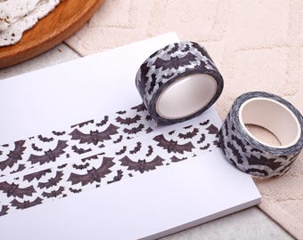 May include: Two rolls of decorative washi tape featuring a bat design. The tape is black and grey, with a repeating pattern of bats. The tape is unrolled on a white surface, showing the bat pattern. Ideal for scrapbooking and crafting projects.