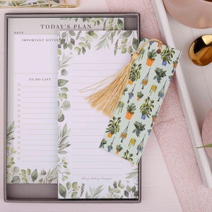 May include: A set of two white lined notepads with a green leafy design and a bookmark with a green leafy design and hanging potted plants. The notepads have the text "Today's Plan" and "To Do List".