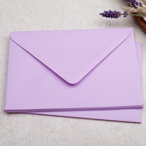 A stack of purple envelopes is placed on a light-colored surface, with a few gold binder clips nearby.