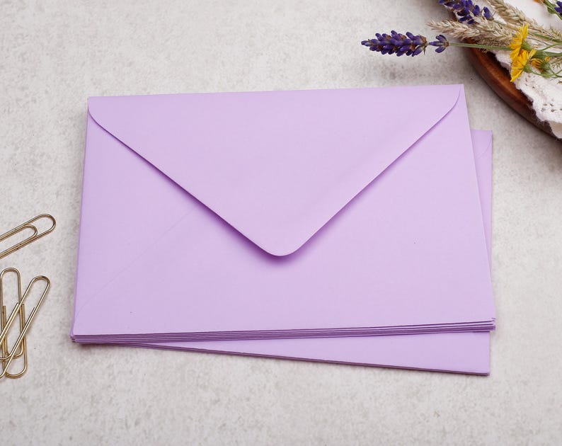A stack of purple envelopes is placed on a light-colored surface, with a few gold binder clips nearby.