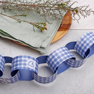 May include: A paper chain garland featuring a blue and white gingham check pattern. The individual circular links are connected to form a continuous strand. Some of the links are decorated with a small white circular sticker displaying a blue heart outline.