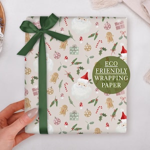 A hand holding a gift wrapped in an eco-friendly wrapping paper with a Christmas-themed design, including Santa Claus, gingerbread men, and other holiday decorations.