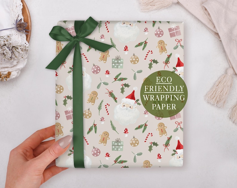 A hand holding a gift wrapped in an eco-friendly wrapping paper with a Christmas-themed design, including Santa Claus, gingerbread men, and other holiday decorations.
