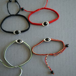 Puede incluir: Cuatro pulseras con cuentas negras y dijes plateados. Las pulseras son rojas, negras, verdes y blancas.