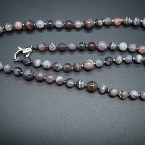 Puede incluir: Un collar hecho de cuentas de ágata gris, blanco y rosa con un cierre plateado.