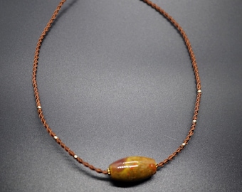 May include: A brown cord necklace with a single, oval-shaped, brown, yellow, and red agate stone bead.