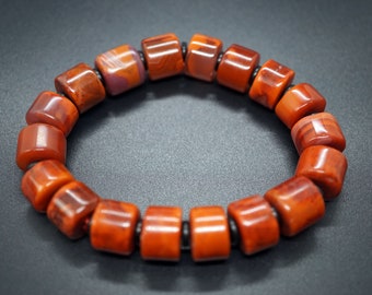 May include: A bracelet made of red and orange stone beads with black accents.