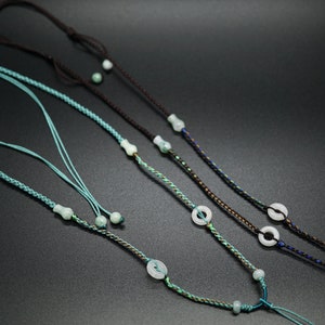 May include: Three necklaces with jade pendants and braided cords. The cords are in shades of brown, blue, and green.