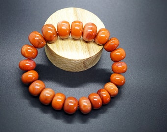 May include: A red carnelian gemstone bracelet with 18 beads. The bracelet is displayed on a wooden stand.