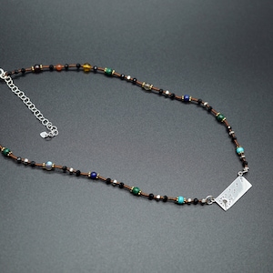 May include: A brown leather cord necklace with a silver pendant featuring a design of birds in flight. The necklace is adorned with small, colourful beads, including black, brown, green, blue, and turquoise.