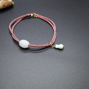 Peut inclure: Un bracelet en cordon tressé rose avec une perle de jade blanche et un pendentif en jade vert.
