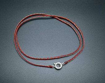 Puede incluir: Un collar de cordón trenzado rojo, azul y dorado con un cierre plateado.