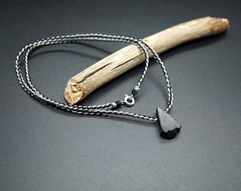 May include: A black wooden pendant shaped like a teardrop hangs from a black and white braided cord necklace.