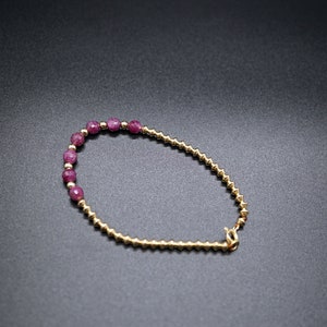 May include: A gold bracelet with a row of pink beads.