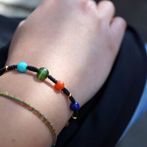 May include: A black string bracelet with five round beads. The beads are turquoise, green, orange, and blue.