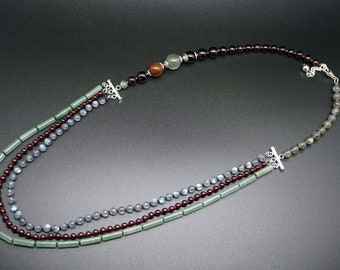 Puede incluir: Un collar de tres hilos con cuentas verdes, azules y rojas. El collar tiene cierres plateados y un conector plateado en el centro.