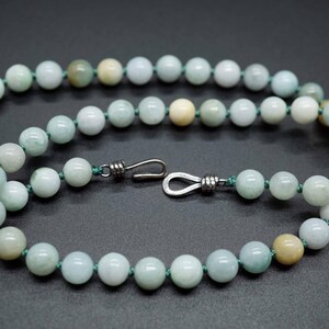 May include: A light green jade bead necklace with a silver clasp. The beads are round and smooth, and the necklace is strung on a green cord.