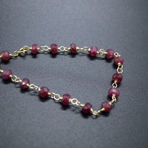 Puede incluir: Un brazalete de cadena dorada con cuentas de piedras preciosas rojas. El brazalete está hecho de pequeñas cuentas facetadas que están conectadas por una delicada cadena dorada.