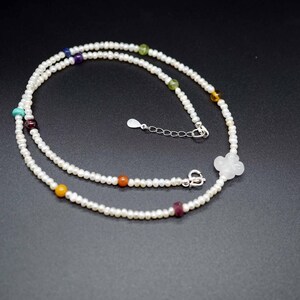 May include: A white pearl necklace with a silver clasp and colorful gemstone beads. The necklace is double-stranded and features a white flower charm.