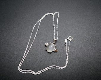 May include: A silver chain necklace with a white oval pendant featuring a small angel design.