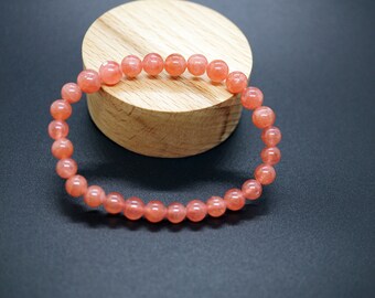 May include: A pink gemstone bracelet with round beads. The bracelet is on a wooden surface.