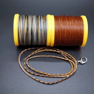 May include: Two spools of thread, one brown and one with a multi-colored pattern, with a brown and white cord with a silver clasp.