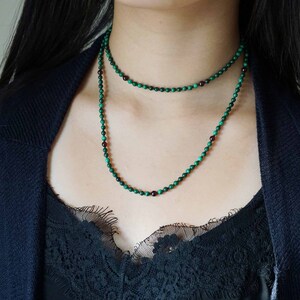 May include: A layered necklace with green and dark red beads. The necklace is made of small, round beads and is worn by a person with long black hair.
