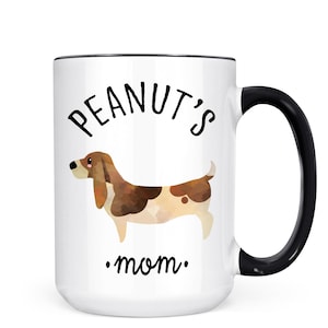 May include: White ceramic mug with a black handle and rim. The mug features the text "Peanut's mom" and a watercolor illustration of a brown and white dog. A perfect gift for dog lovers.