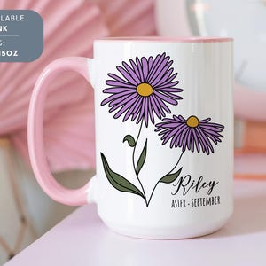 Puede incluir: Taza de cer&aacute;mica blanca con borde y asa de color rosa. La taza presenta una ilustraci&oacute;n de una flor de aster p&uacute;rpura con el nombre "Riley" y el texto "Aster - Septiembre".