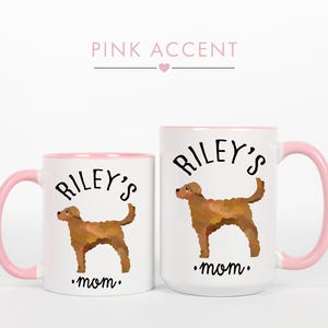 May include: Two white ceramic mugs with pink accents. Each mug features a brown dog illustration and the text "Riley's mom." The mugs have pink handles and rims. The text "Pink Accent" is above the mugs.
