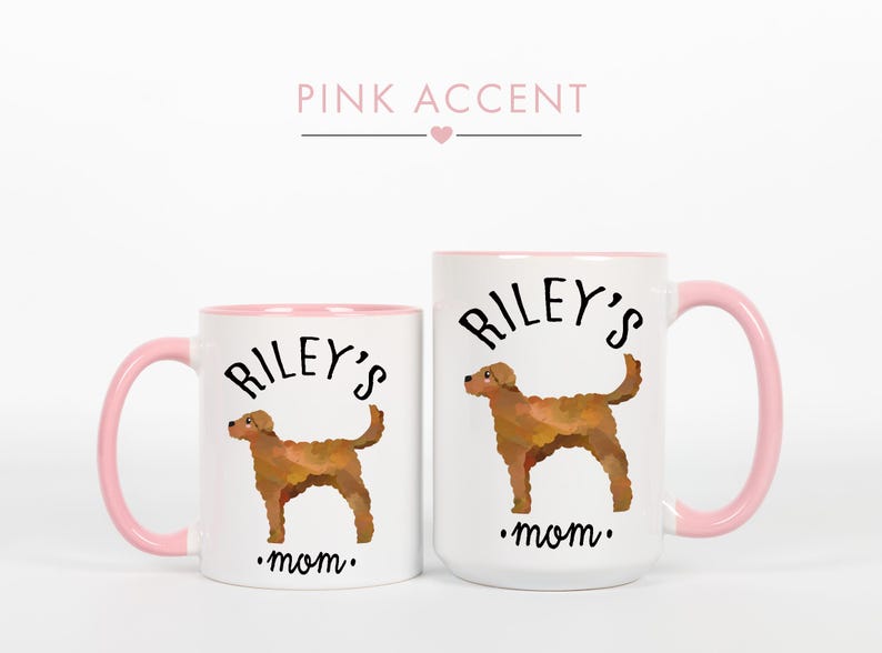 May include: Two white ceramic mugs with pink accents. Each mug features a brown dog illustration and the text "Riley's mom." The mugs have pink handles and rims. The text "Pink Accent" is above the mugs.