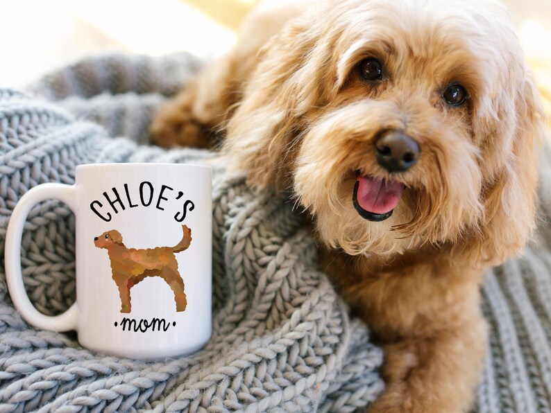 May include: White ceramic mug with the text "CHLOE'S mom" and a brown dog illustration. The mug is on a gray knitted blanket, with a light brown dog in the background.