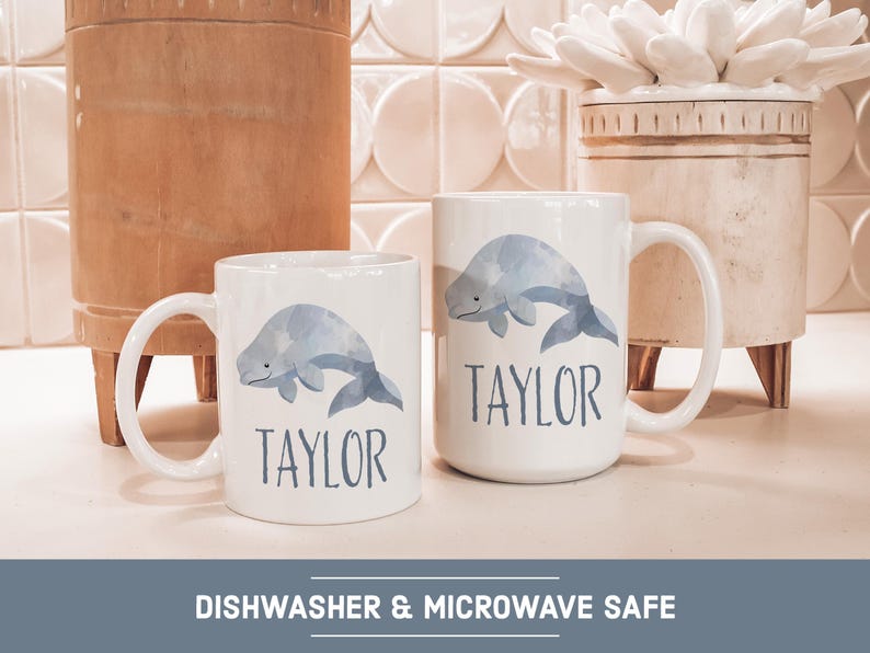 May include: Two white ceramic mugs with a blue whale design and the name "Taylor" printed on each. The mugs are dishwasher and microwave safe.