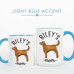 May include: Two white ceramic mugs with light blue accents. Each mug features a brown dog illustration, the text "Riley's" above the dog, and the word "mom" below. The handles and interior rims are light blue.