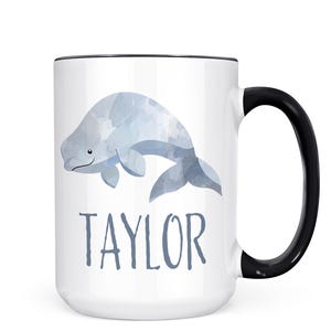 May include: White ceramic mug with a black rim and handle. The mug features a watercolor illustration of a gray whale with the name "TAYLOR" printed below it.
