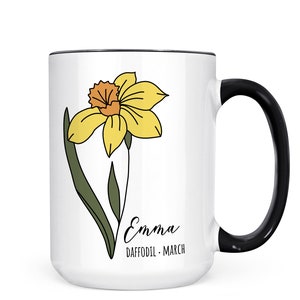 Peut inclure: Mug en c&eacute;ramique blanche avec une anse noire. Le mug pr&eacute;sente un dessin au trait d'un narcisse jaune avec des feuilles vertes et le texte "Emma Daffodil - March".