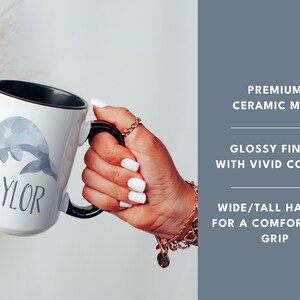 May include: White ceramic mug with a black rim and handle. The mug features a watercolor illustration of a gray whale and the name "TAYLOR" printed in gray text.