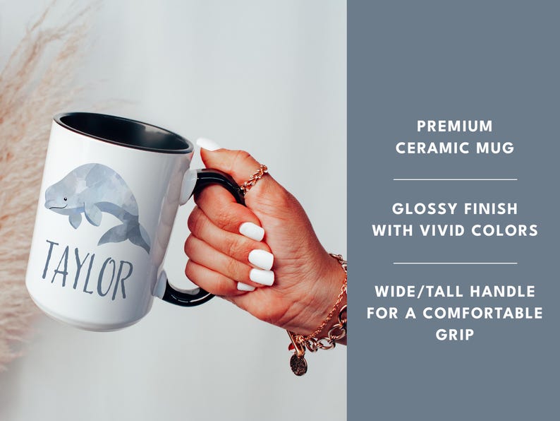 May include: White ceramic mug with a black rim and handle. The mug features a watercolor illustration of a gray whale and the name "TAYLOR" printed in gray text.