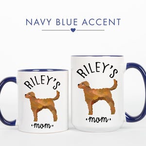 May include: Two white ceramic mugs with navy blue accents. Each mug features a brown dog illustration and the text "Riley's mom." The larger mug has a capacity of approximately 15 ounces.