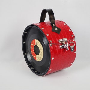 Könnte beinhalten: Eine rote Schallplatten-Handtasche mit einem schwarzen Ledergriff und silbernen Akzenten. Die Tasche ist mit silbernen Nieten verziert und hat ein Kroko-Prägemuster.