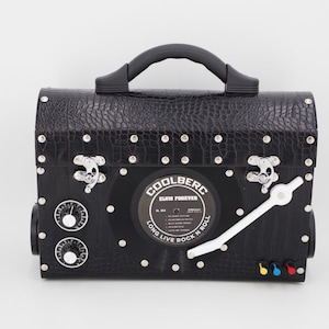 May include: Black faux leather bag with a vinyl record on the front that says "COOLBERG ELVIS FOREVER LONG LIVE ROCK N ROLL". The bag has a silver handle, silver clasps, and silver studs. There are two silver knobs on the side of the bag.