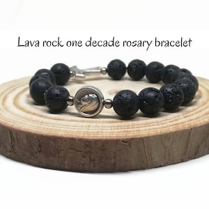 Può includere: Braccialetto da rosario in pietra lavica nera con un ciondolo d'argento. Il braccialetto è su una superficie di legno.