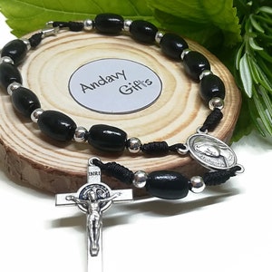May include: A black wooden bead rosary bracelet with silver-coloured accents and a crucifix. The bracelet is displayed on a small wooden slice with the text "Andavy Gifts".