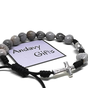 Puede incluir: Pulsera de cuentas grises con un dije de cruz plateada. La pulsera presenta cuentas redondas grises y un cordón negro. La etiqueta en la imagen dice "Andavy Gifts".