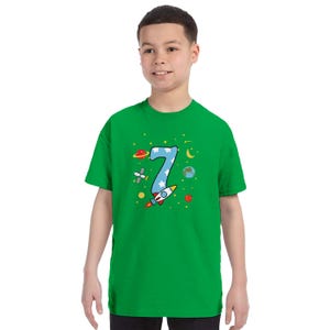 May include: A green t-shirt featuring a number 7 in blue with white stars, a rocket ship, planets, and other space-themed graphics. The shirt is a short-sleeved crew neck.