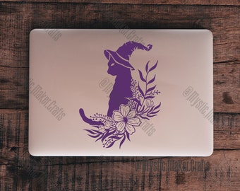 May include: Purple silhouette of a cat wearing a witch's hat with floral accents on a light gray laptop.