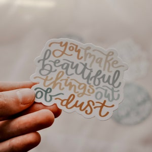 May include: A white sticker with the text "You make beautiful things out of dust" written in a colorful, handwritten font.