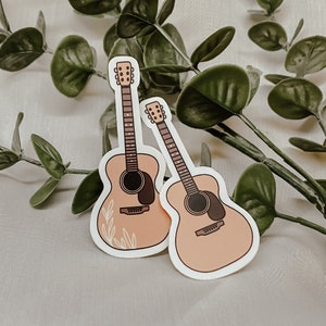 Pode incluir: Dois adesivos de guitarra ac&uacute;stica cor de p&ecirc;ssego com detalhes marrons. As guitarras t&ecirc;m um design floral no corpo.
