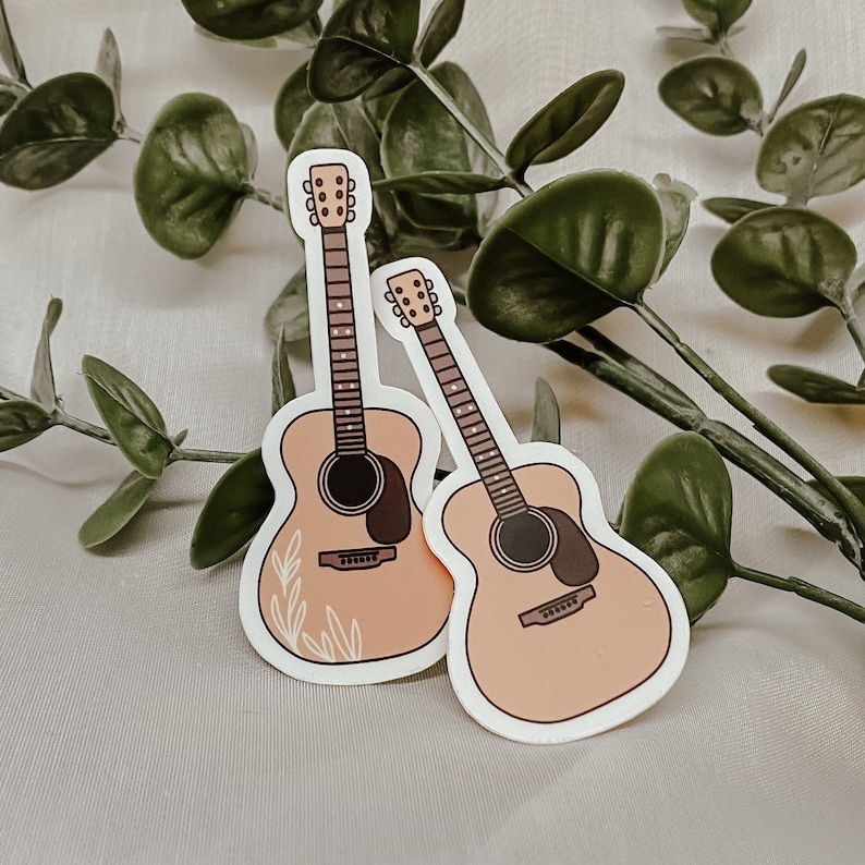 Pode incluir: Dois adesivos de guitarra ac&uacute;stica cor de p&ecirc;ssego com detalhes marrons. As guitarras t&ecirc;m um design floral no corpo.
