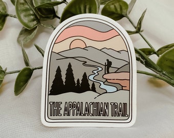 May include: A sticker with a retro illustration of a mountain range, a winding river, and two hikers. The sticker is white with a gray border and the text "THE APPALACHIAN TRAIL" in black.